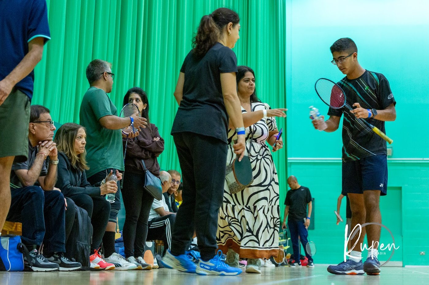 Badminton players and families waiting courtside with rackets