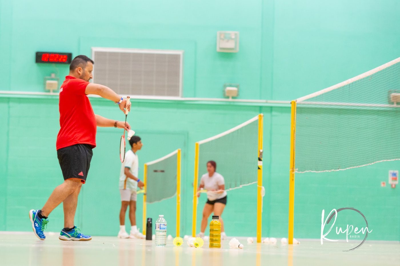 A badminton player reaching for a shot on the sports hall courts