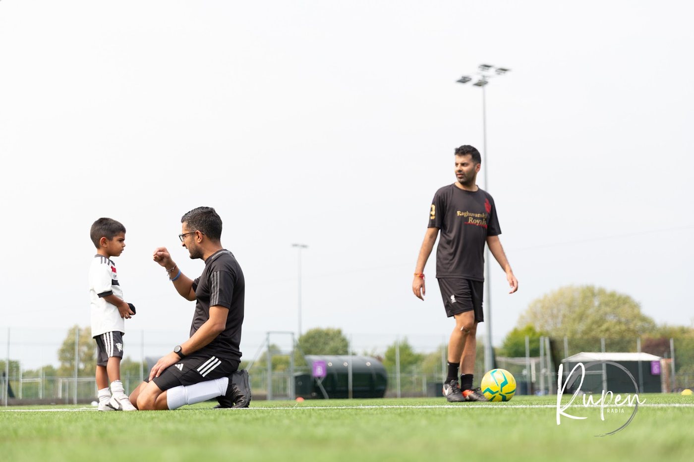 A coach kneeling to talk to a young player on the 3G football pitch