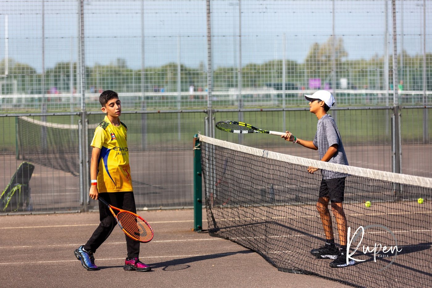 Two junior players either side of the net on the outdoor tennis courts