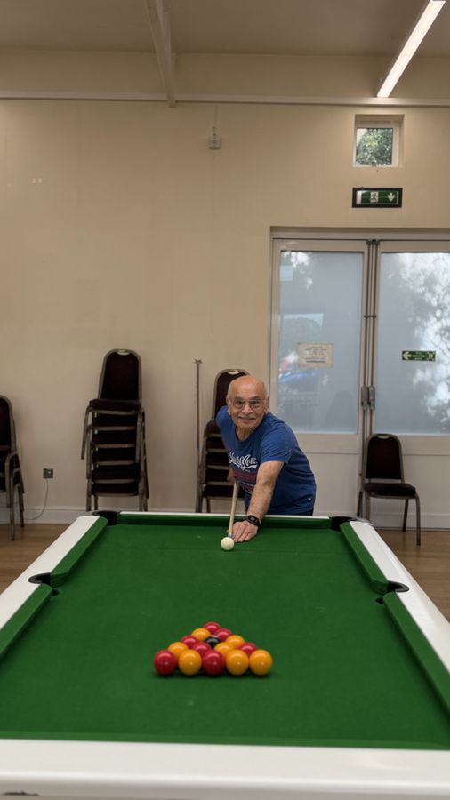 An older player leaning over a pool table to take the opening break of a frame