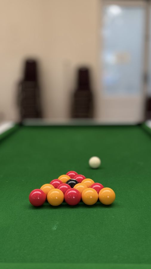 A triangle of red and yellow pool balls racked on green baize ready to break