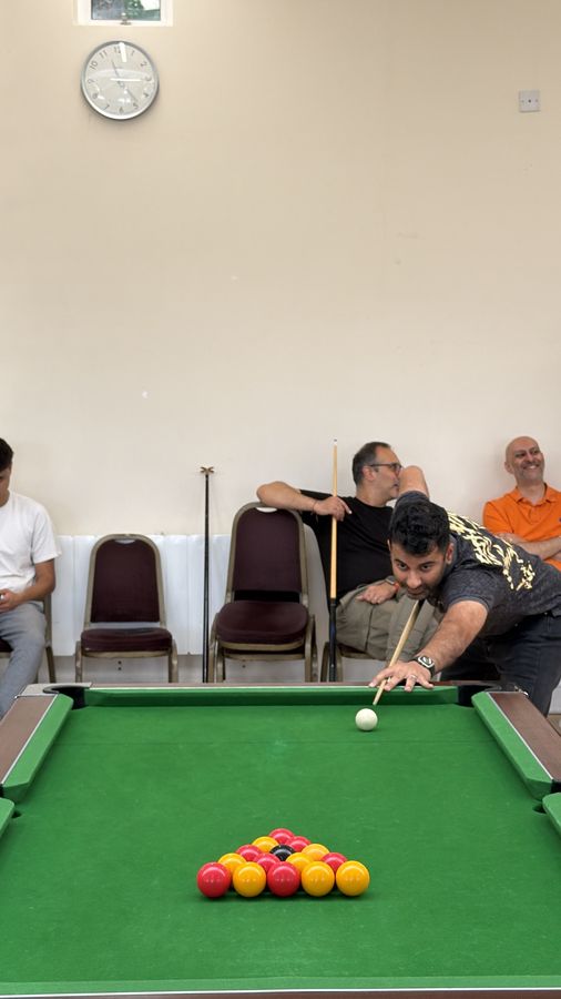 A player taking a shot while three spectators watch from chairs behind the table