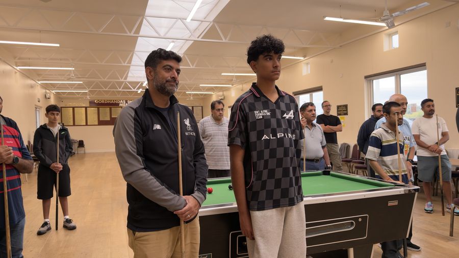An adult and a teenage player standing side by side with cues beside a pool table in Harrow