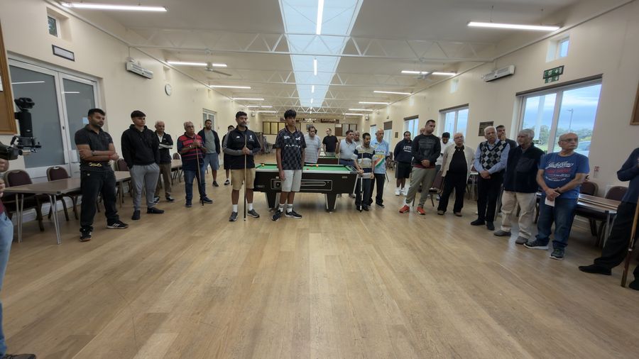 Players and spectators gathered around the first pool table of the day in a ring