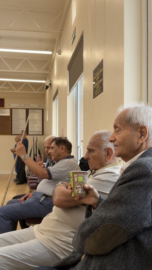 Older members of the Lohana community watching the pool with cups of tea
