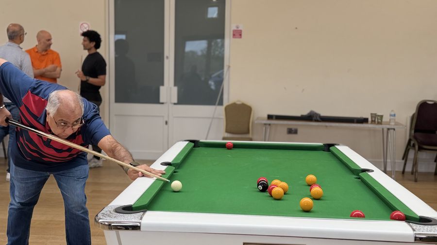An Over 50 singles player lining up a shot at a pool table in Harrow