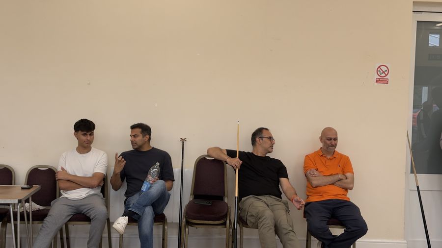 Four members sitting against the wall watching the pool tournament between matches