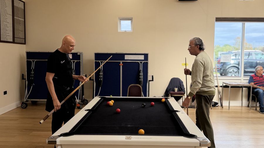 Two players standing either side of a black-cloth pool table between shots at the RCT Centre