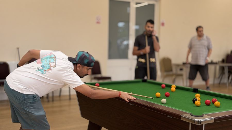 A player in a cap down low on the cue lining up a shot while opponents watch