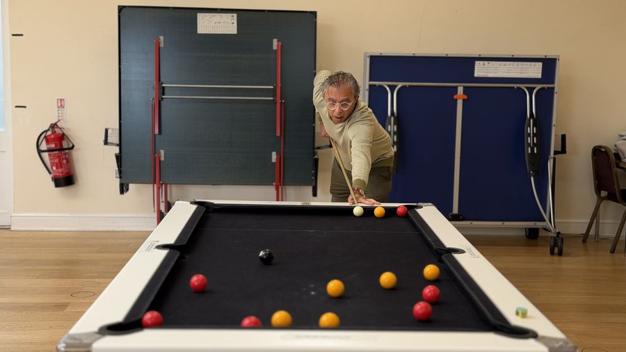 An Over 50 player leaning in to play a shot on a black-cloth pool table in Harrow