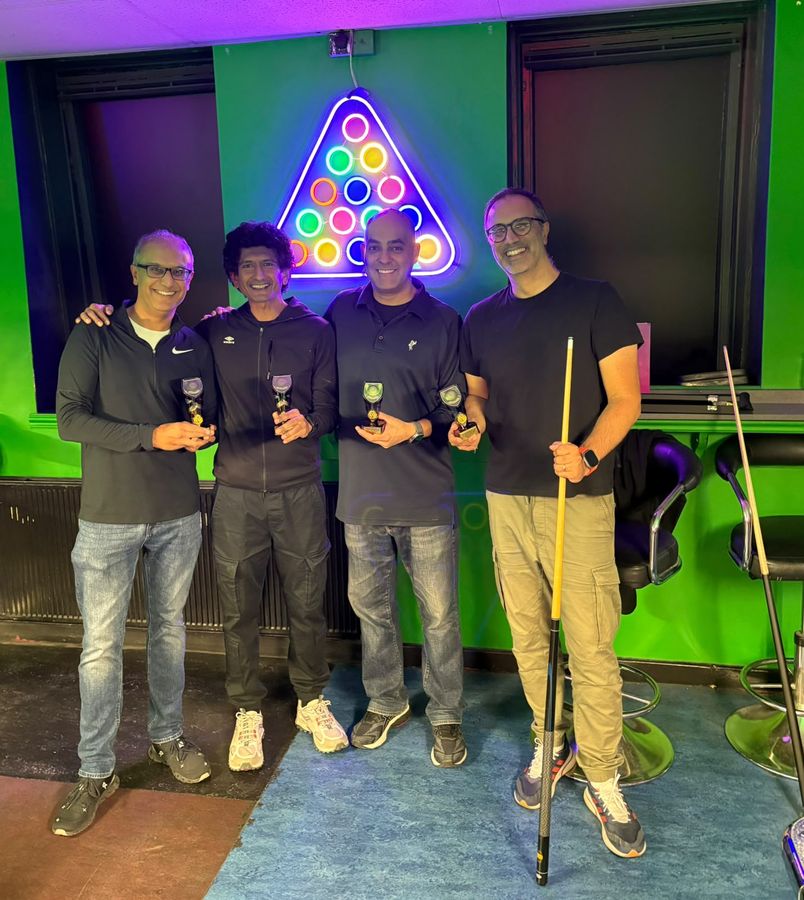 The four Open Doubles finalists, Biral Devani, Paras Patani, Neil Morjaria and Shenal Devani, holding their trophies under a neon pool rack sign